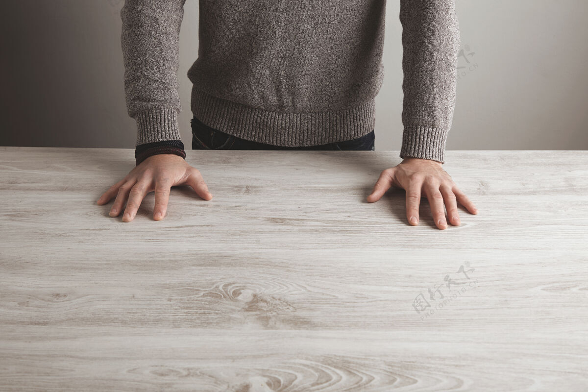 桌子穿灰色毛衣的男人把手放在空白的白色木桌上 孤立在简单的墙上最小木头手