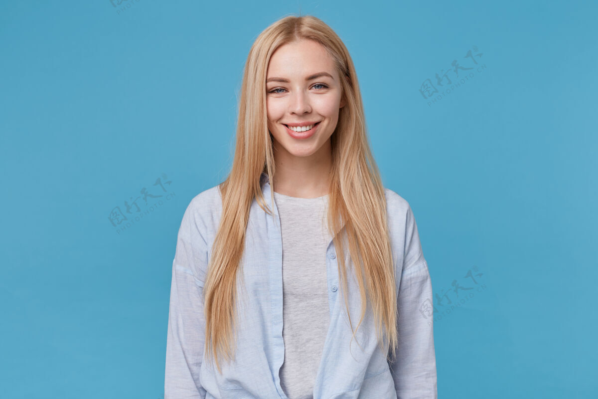 快乐可爱的年轻长发女子 身穿蓝色衬衫和灰色t恤 双手放在身上 欢快地微笑着表情情绪心情