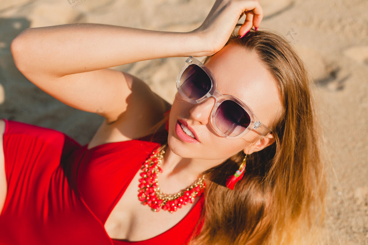 女人年轻漂亮的金发女人穿着红色泳衣 戴着墨镜在沙滩上晒太阳时尚脸夏天