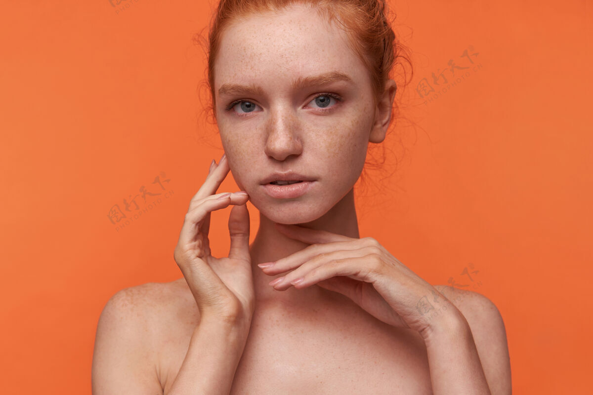 柔软优雅的年轻女士 一头浓密的头发 不化妆 举手轻抚脸颊 在橙色背景上摆姿势漂亮结20多岁