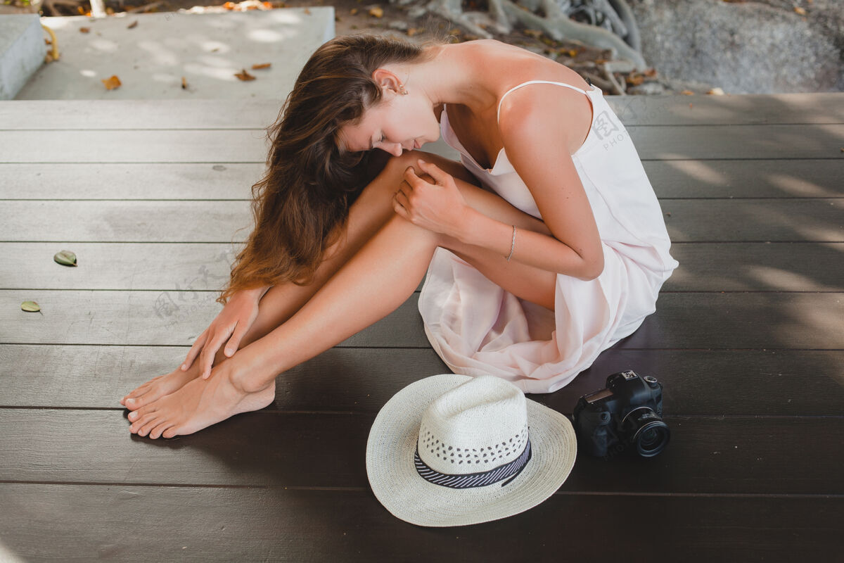 年轻年轻女子光着脚坐在地板上 穿着苍白的连衣裙 微笑着 自然美丽 草帽 数码相机 摄影数码微笑