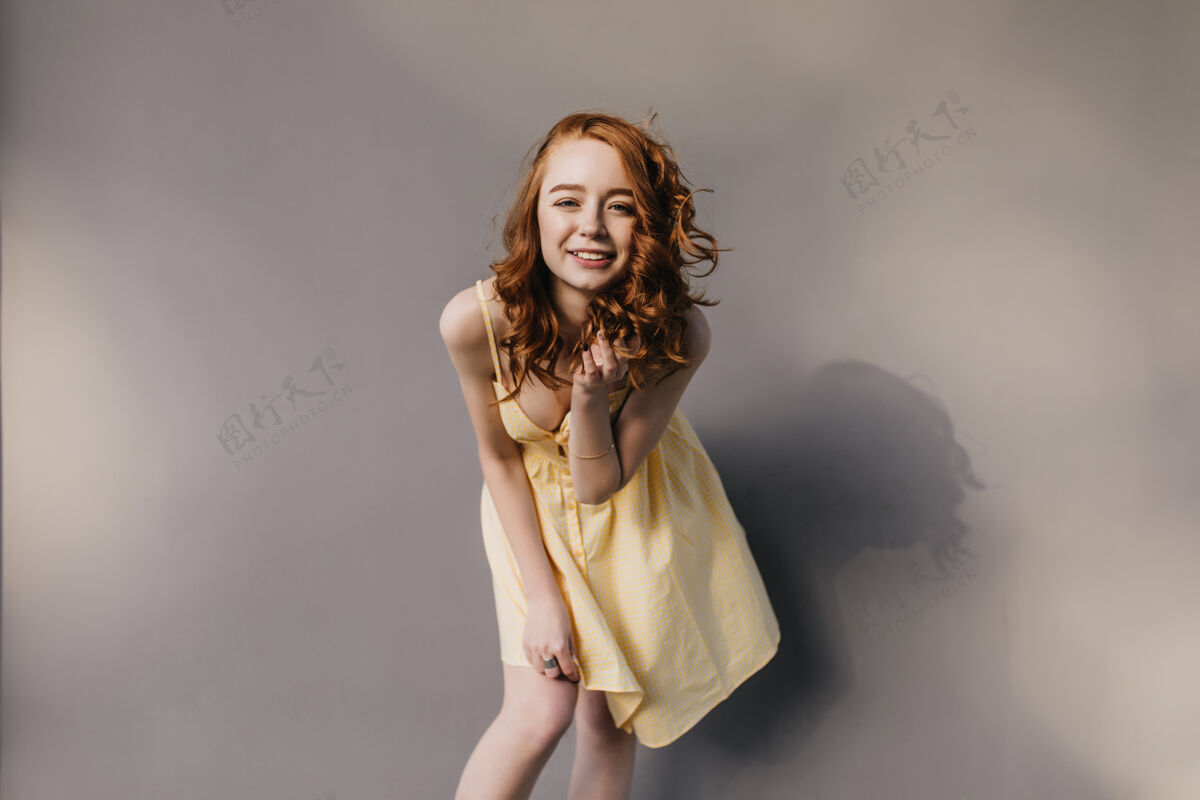 成人迷人的卷发女孩穿着时髦的黄色连衣裙笑着姜女在拍照时玩得很开心跳舞年轻姜