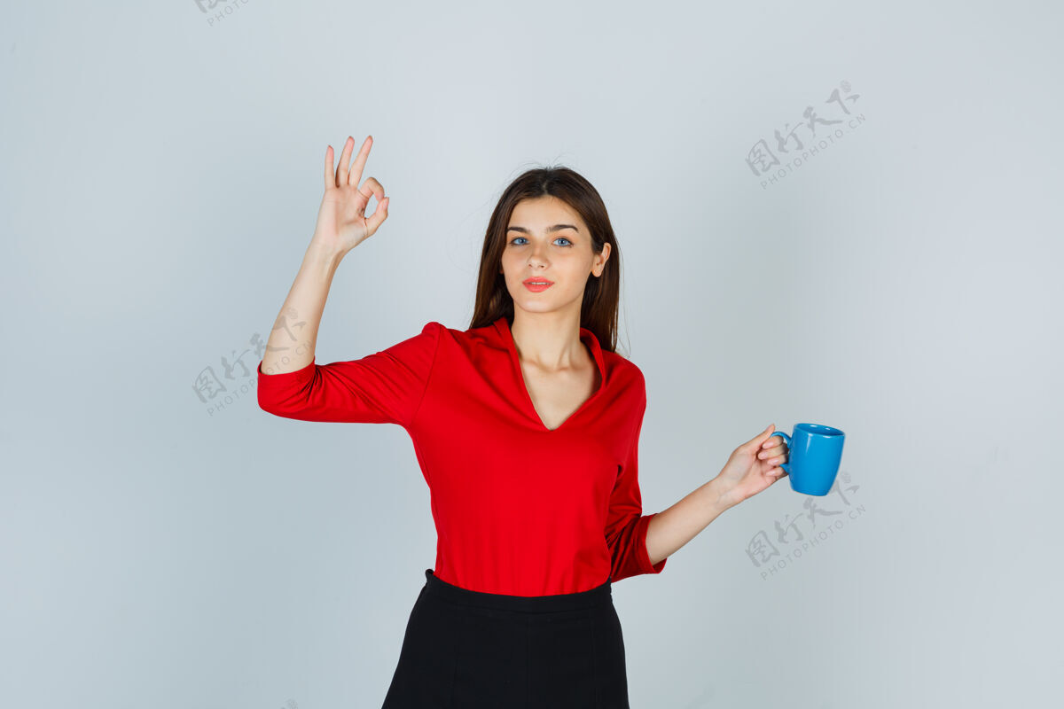 成功穿红衬衫的年轻女士 拿着杯子的裙子 摆着ok的姿势人人商务女性