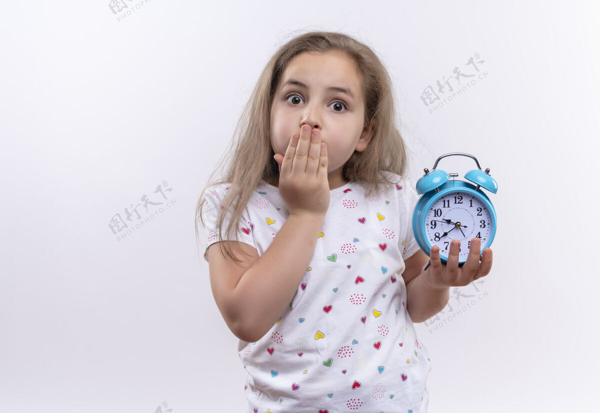拿着惊讶的小女生穿着白色t恤拿着闹钟捂着嘴孤立的白色背景学校盖着时钟