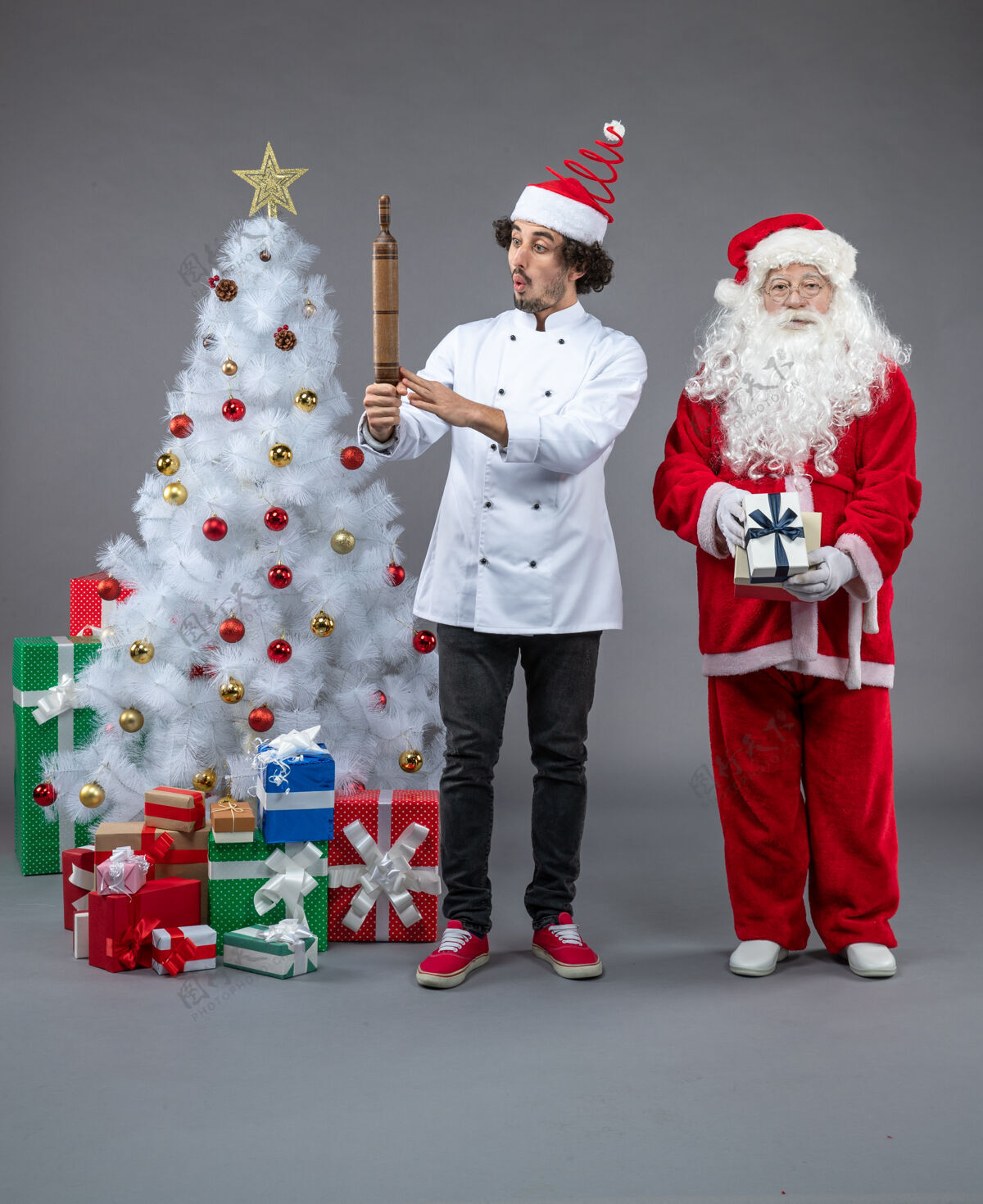 微笑圣诞老人和男厨师在灰色墙上围着圣诞礼物的正视图圣诞老人庆祝人