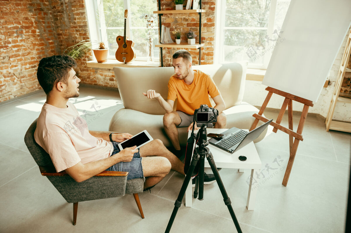 年轻人两位年轻的白人男性博主穿着休闲服 在家里用专业设备或摄像机录制视频采访博客 视频博客 视频博客在室内直播时聊天内容视频博客流