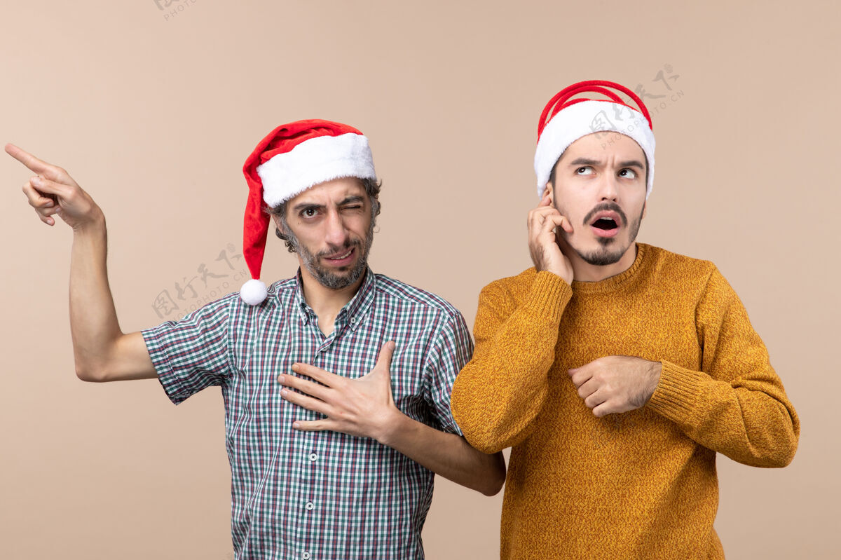 前面前视图两个圣诞老人戴着圣诞帽的家伙一个在展示一些东西 另一个在米色孤立的背景上思考两个伙计们观点