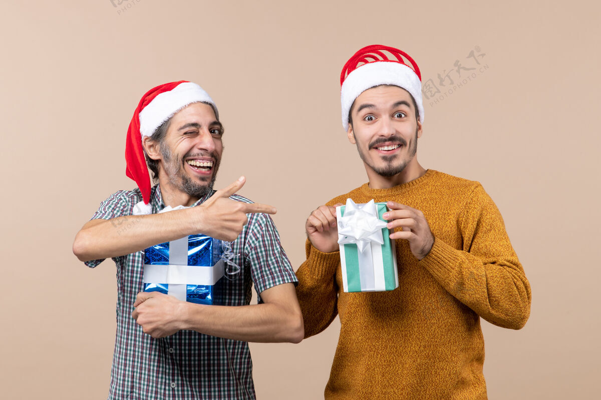 戴着正面图：两个戴着圣诞帽 拿着礼物的快乐的家伙在孤立的背景下两个男帽子