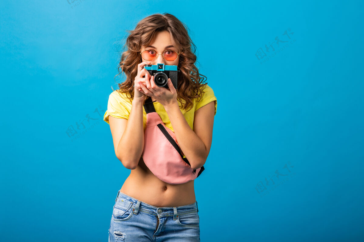 情感可爱的女人用老式相机拍照 穿着时髦的夏季彩色套装 隔离在蓝色背景上 隐藏着惊讶的表情肖像兴奋蓝色