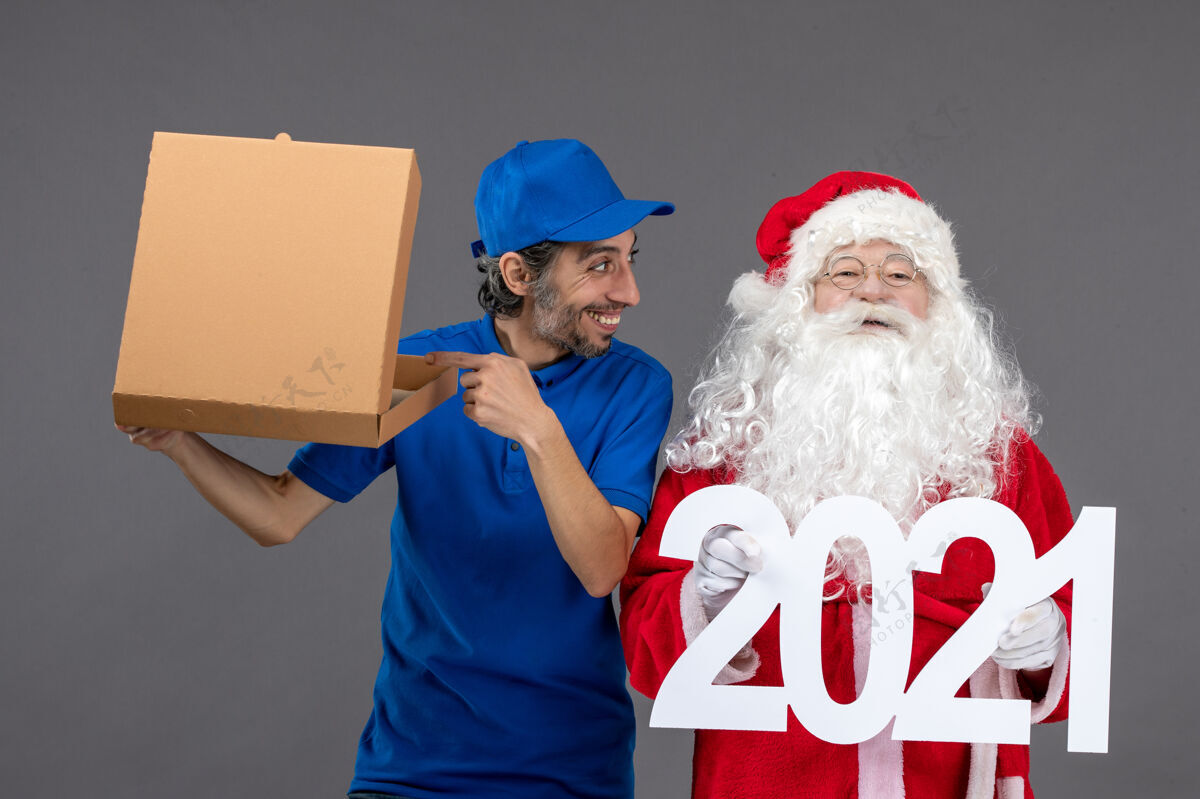 人圣诞老人的正面图 灰色的墙上有男信使拿着购物袋和食品盒圣诞老人快乐圣诞