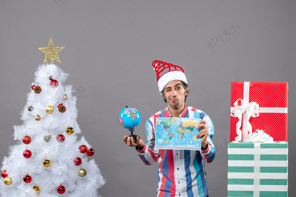 人前视图失望的男子与螺旋弹簧圣诞帽举行世界地图和地球仪微笑人圣诞树