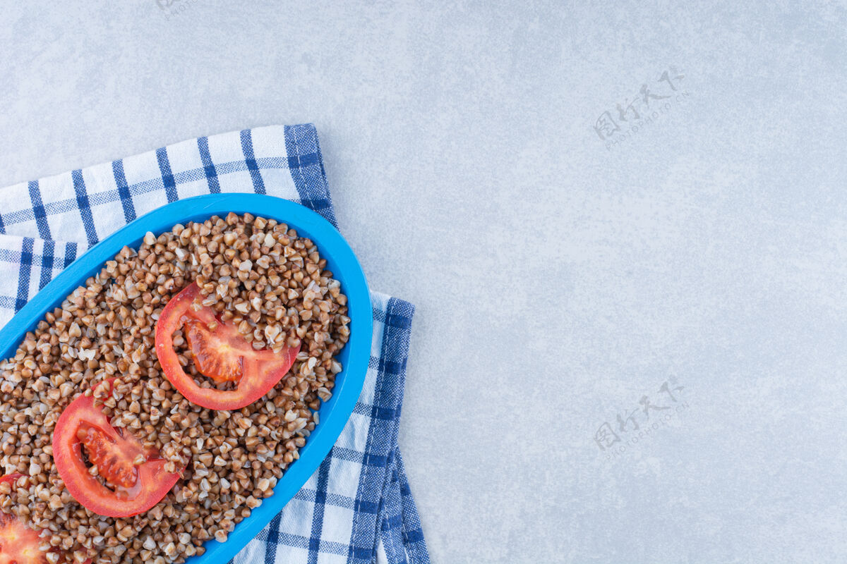 切片新鲜的番茄片装饰一盘熟荞麦在折叠毛巾大理石背景上熟的有机番茄