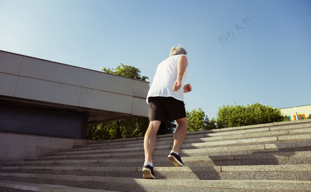 慢跑在城市街道上戴着臂章或健身跟踪器的高级男子跑步者高加索男模在夏天的早晨练习慢跑和有氧训练健康的生活方式 运动 活动理念运动员运动草地