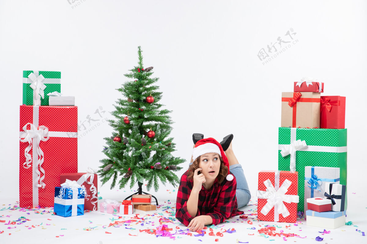 庆祝年轻女子躺在白色墙壁上的圣诞礼物和小圣诞树周围的正视图女人冬青节日