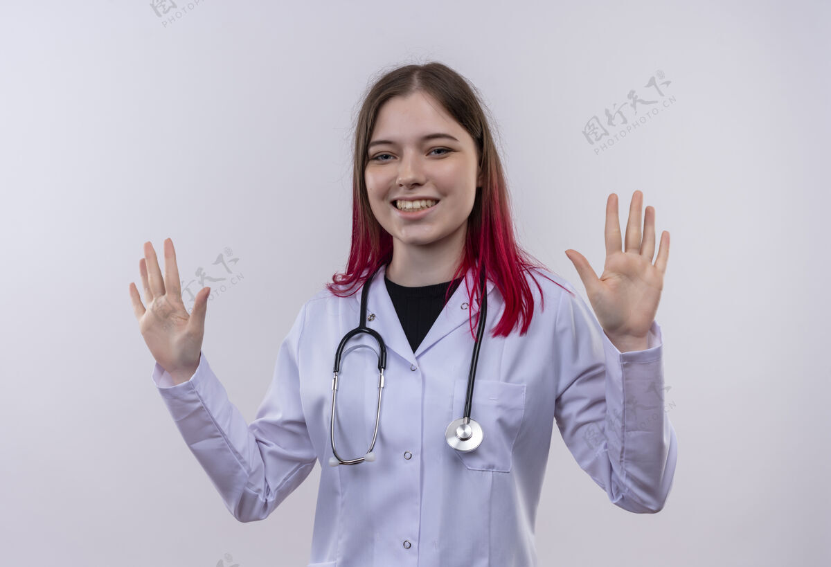 穿着微笑的年轻医生女孩穿着听诊器医用长袍 在孤立的白色背景上举手微笑提高手