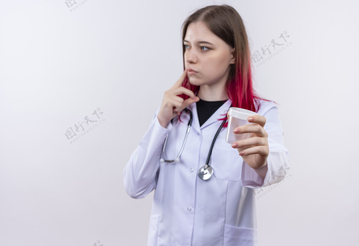 侧着看着身边年轻的女医生穿着听诊器医用长袍 拿着空罐子对着镜头对着孤立的白色背景抱着女孩医生