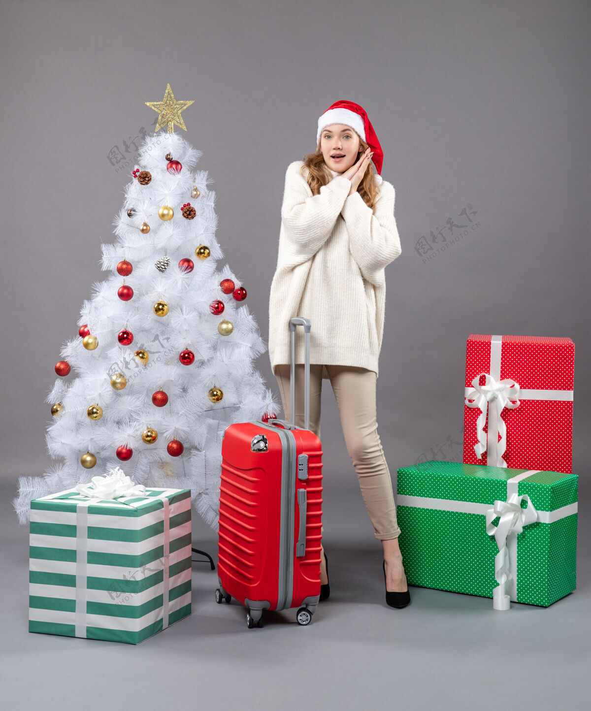 人前视图惊讶的女孩戴着圣诞帽站在白色圣诞树和礼品盒附近惊奇女孩站着圣诞树