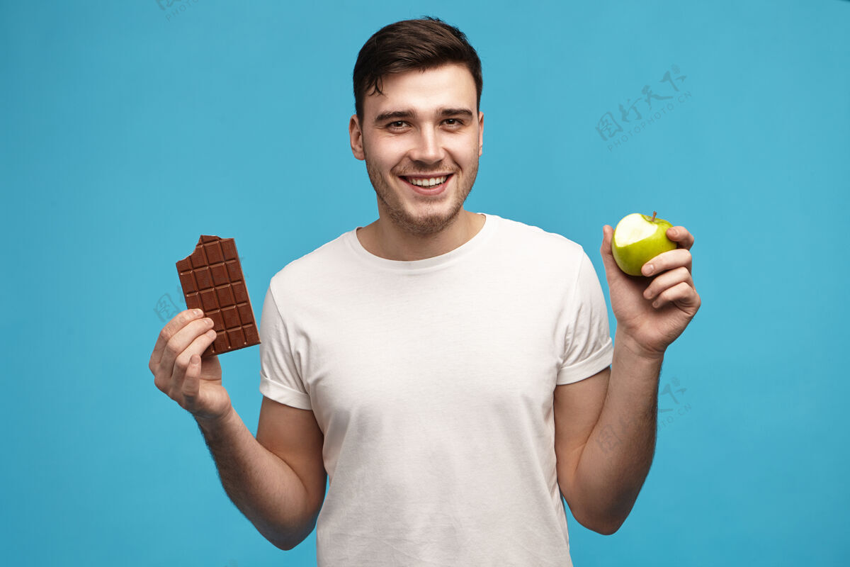 糖果快乐的年轻黑发小伙子抱着半咬的青苹果 带着激动的笑容看着镜头零食男孩青春期