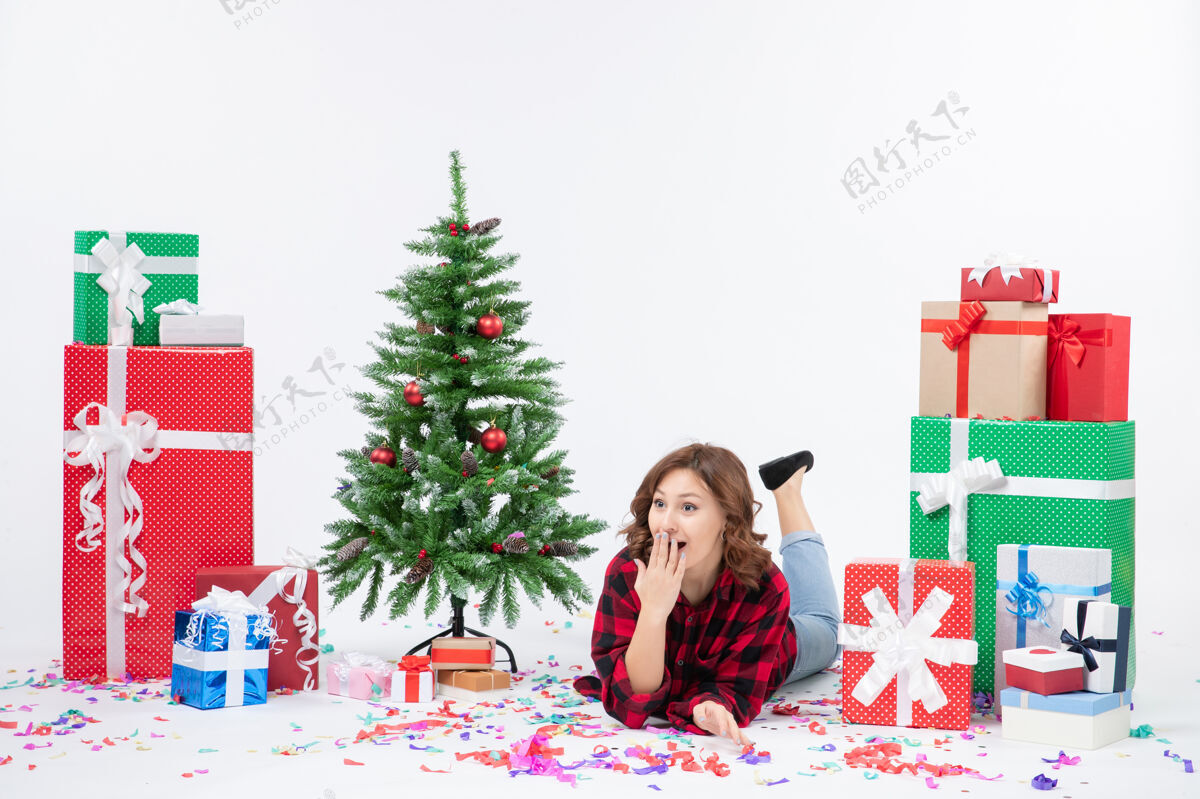 年轻正面图年轻女性躺在白色背景上的圣诞礼物和圣诞树上 圣诞礼物颜色雪白感慨女性树躺着