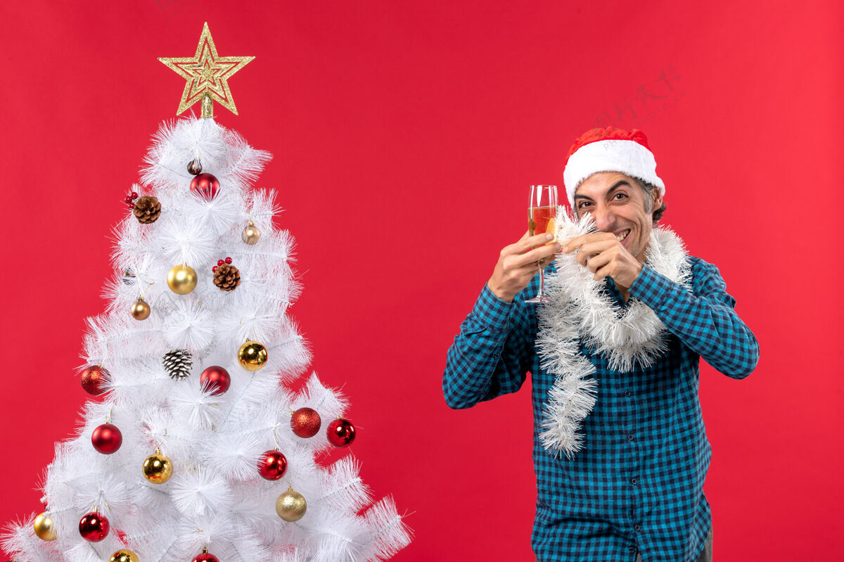 新年前夜圣诞气氛与疯狂的年轻人圣诞老人帽子和提高一杯葡萄酒欢呼自己附近的圣诞树年玻璃新