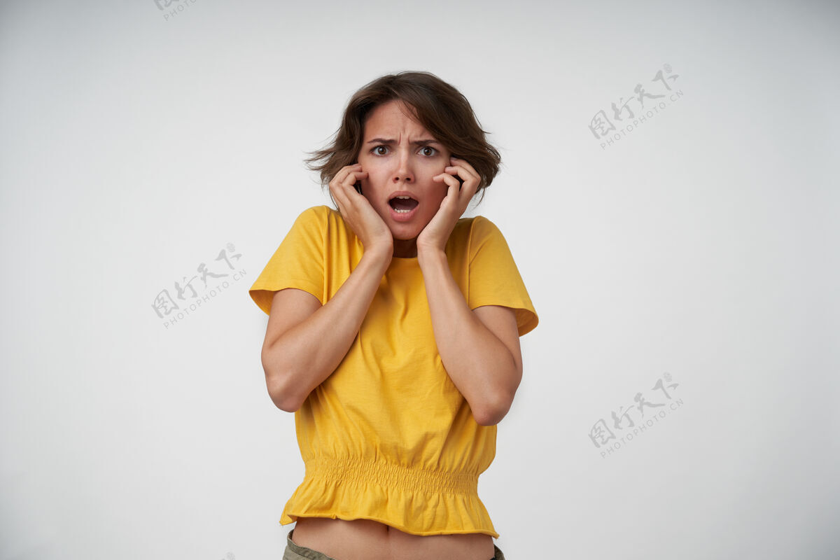 女性时髦的年轻短发女性 站着的时候穿着黄色的t恤 表情困惑 眉头紧锁 手放在脸上抱着女士脸