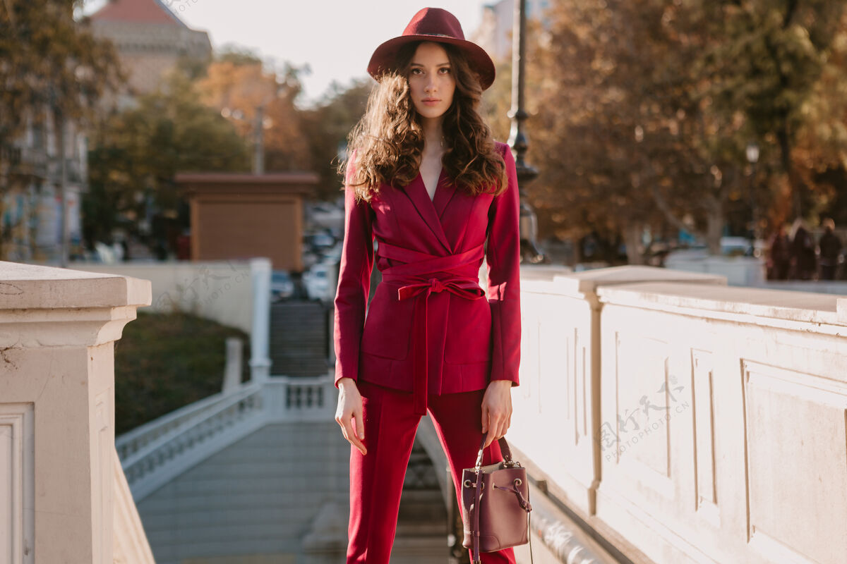 阳光穿着紫色西装的漂亮时髦女人走在城市街头 春夏秋冬时节时尚潮流戴着帽子 手拿钱包女士深色漂亮
