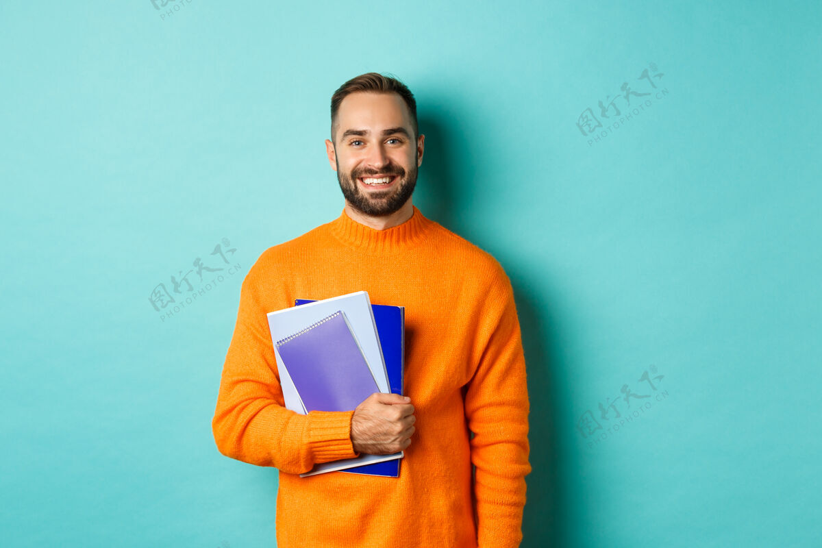 手势微笑的胡须男人拿着笔记本 微笑着 继续上课 站在浅蓝绿色的墙上现代胡须成年人