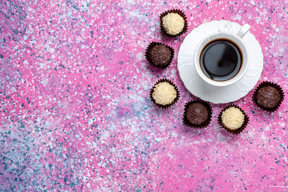 糖果顶视图美味的巧克力糖果白色和黑色巧克力与茶杯的粉红色背景茶甜顶
