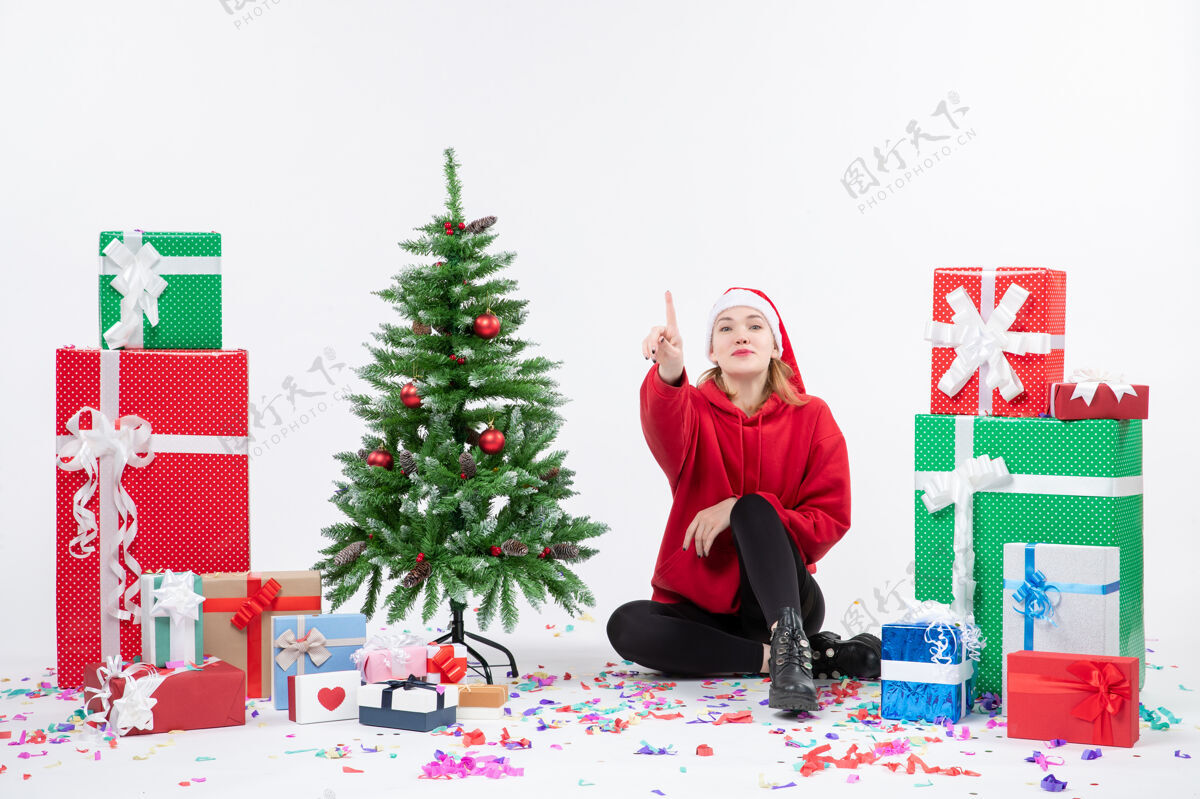 庆祝年轻女子坐在白色墙壁上数着节日礼物的前视图圣诞快乐人人