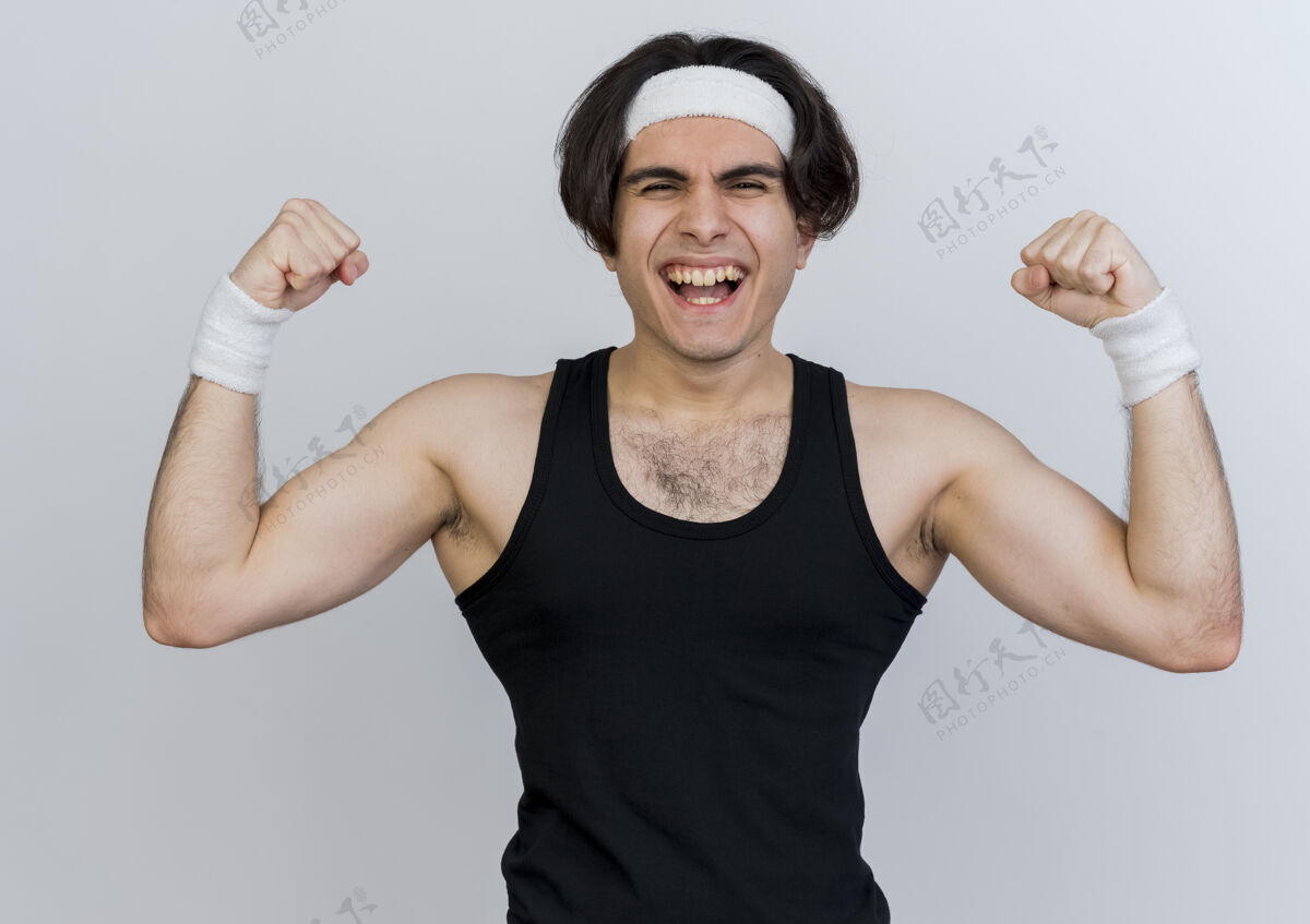长相年轻的运动型男子穿着运动服和头带举起拳头显示力量和二头肌看起来紧张快乐和积极的举起力量拳头