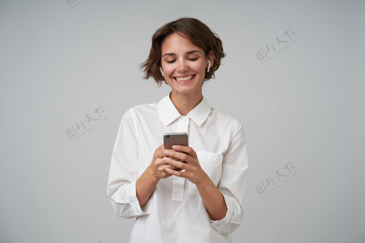 积极快乐的年轻黑发女士高举着手机 站着穿着正式的衣服 高兴地看着屏幕欢快抱着肖像
