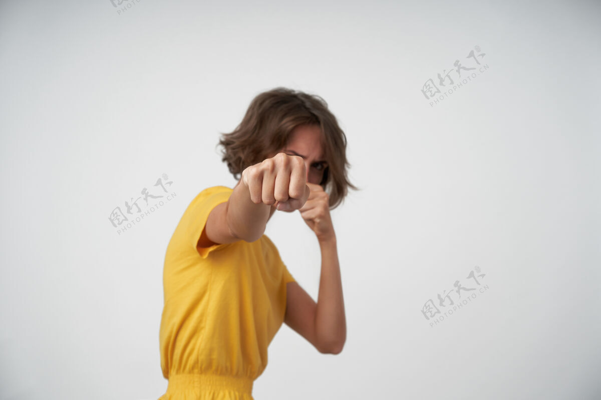 漂亮室内拍摄的年轻黑发女子穿着黄色t恤 站着举起拳头 打着休闲发型打拳击情绪衣服严肃