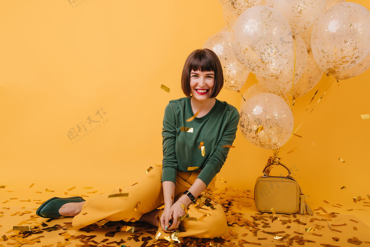 微笑幸福的白人女孩笑着看着金色的五彩纸屑快乐的棕发模特在生日派对上玩得很开心的室内照片年轻气球有趣