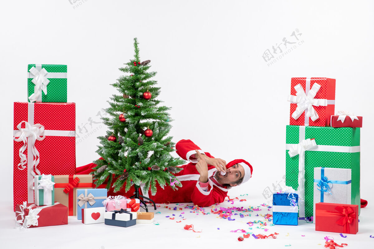 礼物喜庆的节日气氛与年轻的圣诞老人躺在圣诞树后 靠近礼物的白色背景图片圣诞老人盒子圣诞老人
