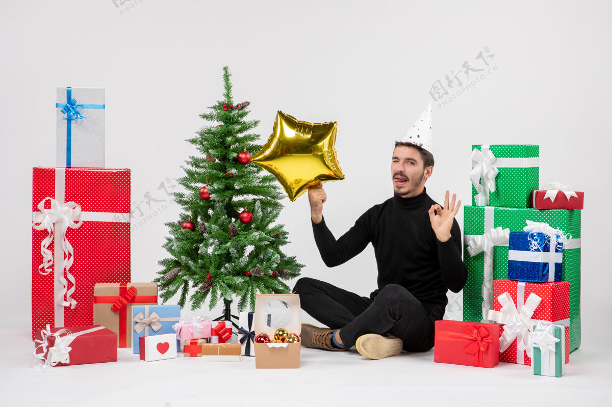 坐着正面图：年轻人围坐在礼物旁边 手里拿着白色墙上的金星圣诞节圣诞快乐人