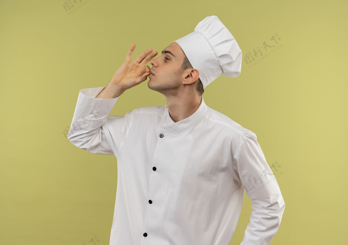 展示站在剖面图年轻的男厨师穿着厨师制服显示出美味的姿态与复制空间制服厨师手势