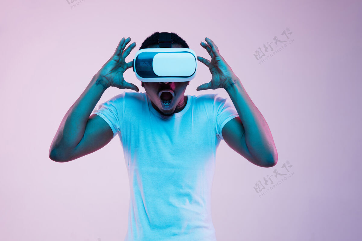开朗年轻人戴着虚拟现实眼镜在霓虹灯下玩成功情绪面部