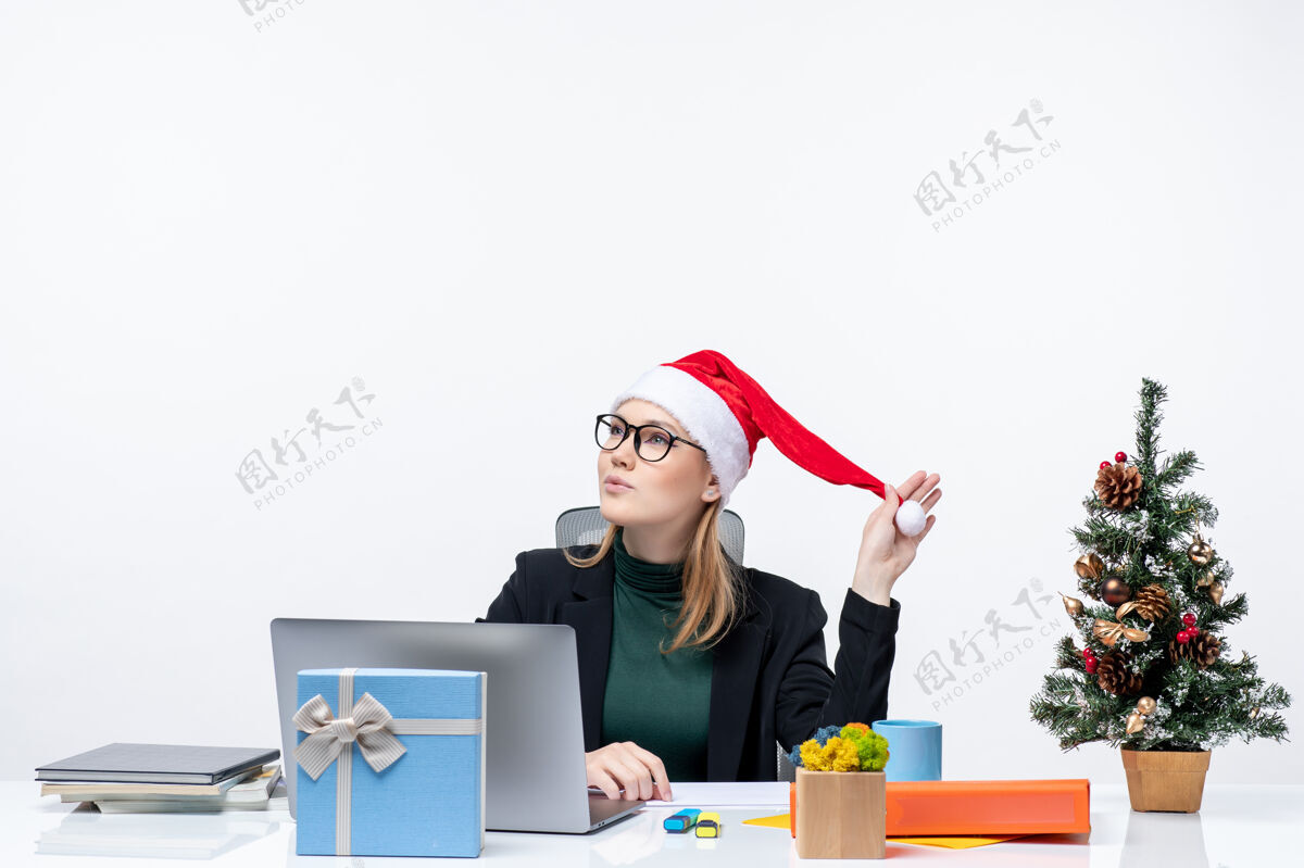 金发女郎新年气氛与梦幻积极的金发女人坐在一张桌子上 圣诞树和一个白色背景的礼物圣诞老人帽子梦幻女郎女商人圣诞老人