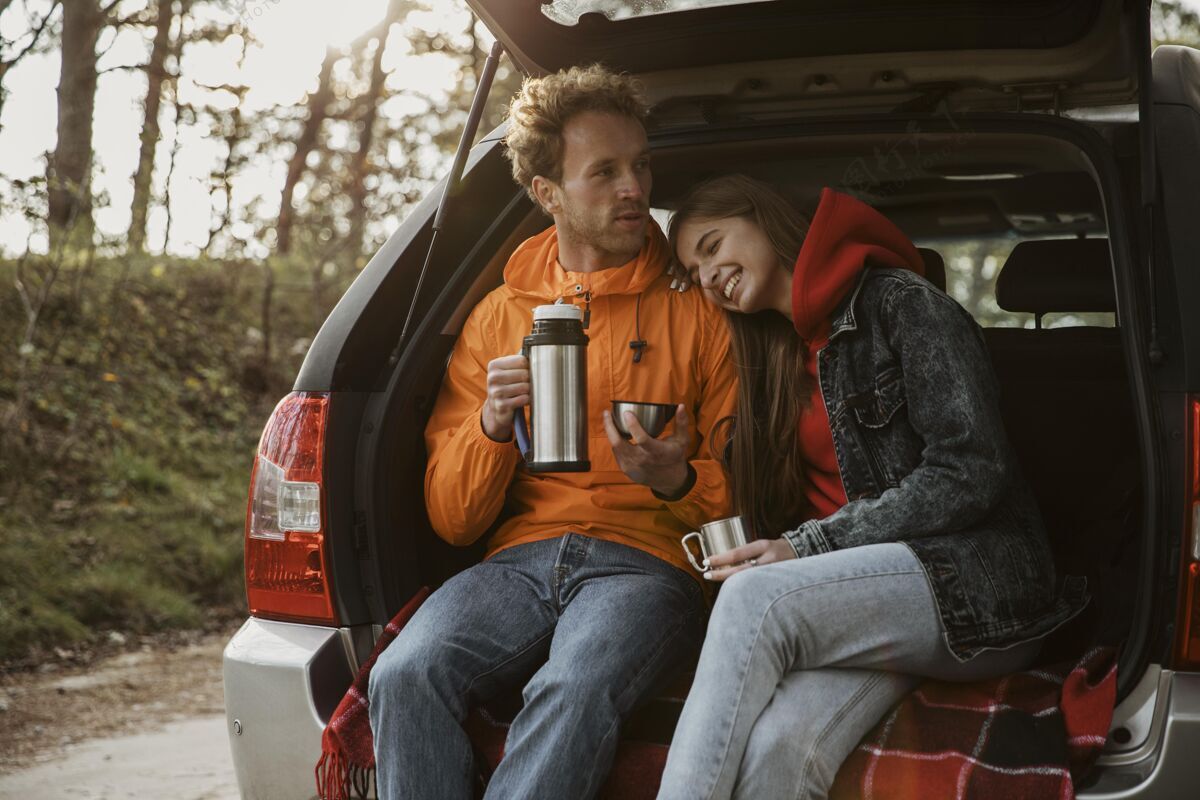 冒险一对夫妇在汽车后备箱里享用热饮料的前视图男性女性远足