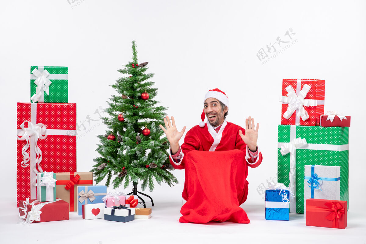 圣诞老人快乐的年轻人打扮成圣诞老人与礼物和装饰圣诞树上的白色背景打扮微笑圣诞老人