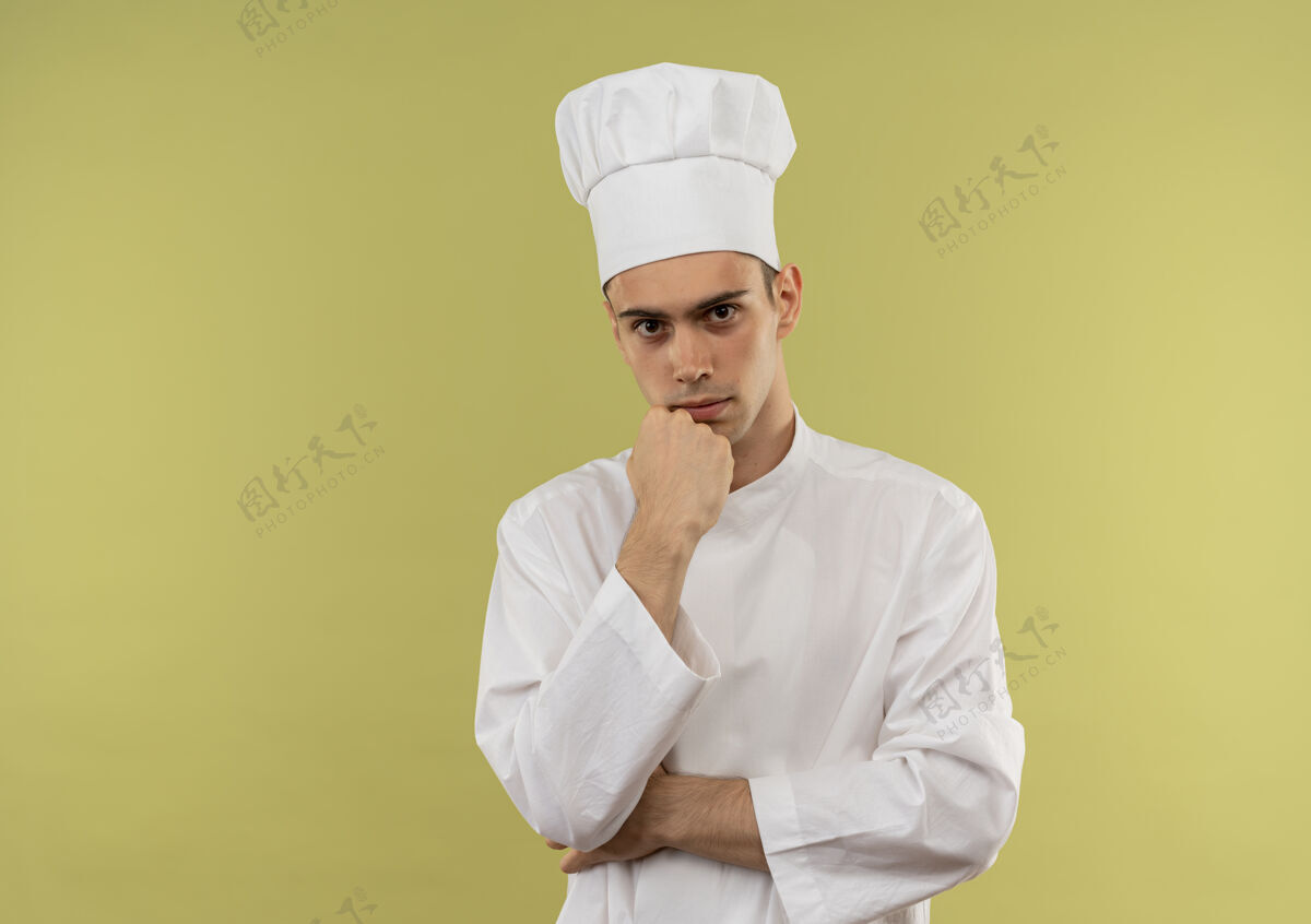 穿自信的年轻男厨师穿着厨师制服 将手放在下巴下 放在隔离的绿色墙壁上 留有复制空间制服下巴看起来