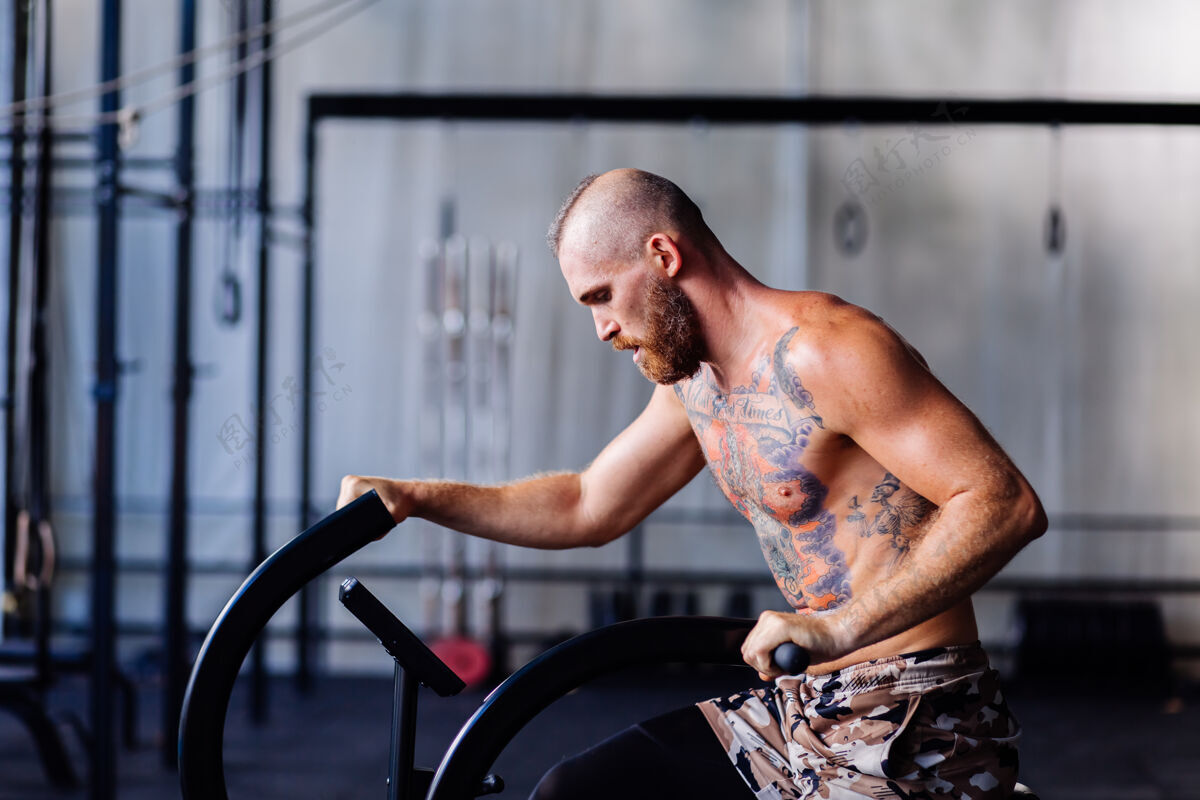空气帅哥纹身壮汉在健身房做有氧运动自行车锻炼身体