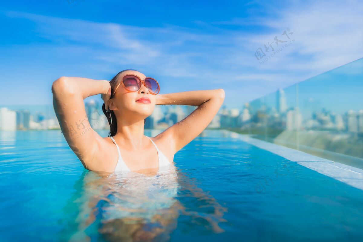 无限肖像美丽的亚洲年轻女子微笑放松休闲围绕室外游泳池与城市景观梦想度假村高