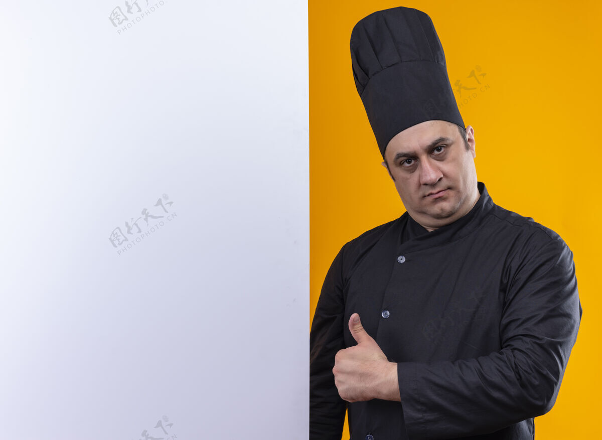 墙自信的中年男厨师 身着厨师制服 手举白墙 大拇指竖立在黄色墙上 留有复印空间厨师厨师抱着