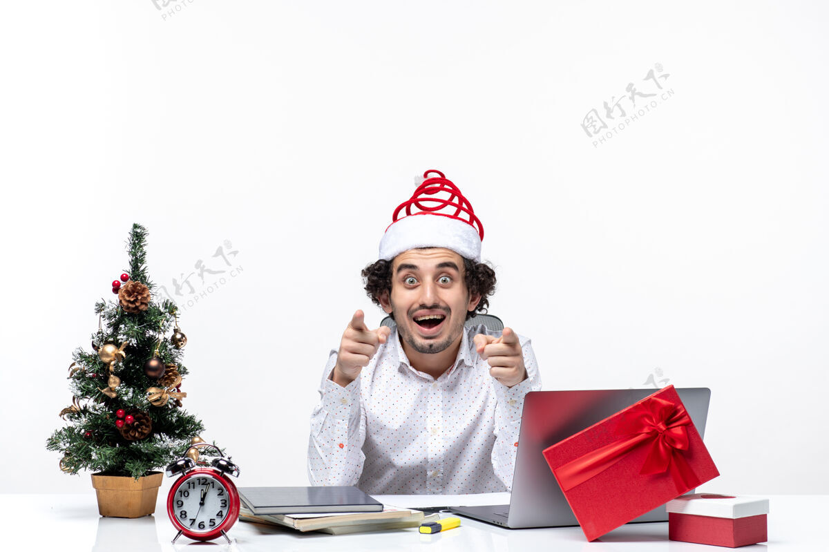 成年人好奇的年轻商人戴着滑稽的圣诞老人帽 在白色背景下询问办公室里的一些事情微笑办公室礼物