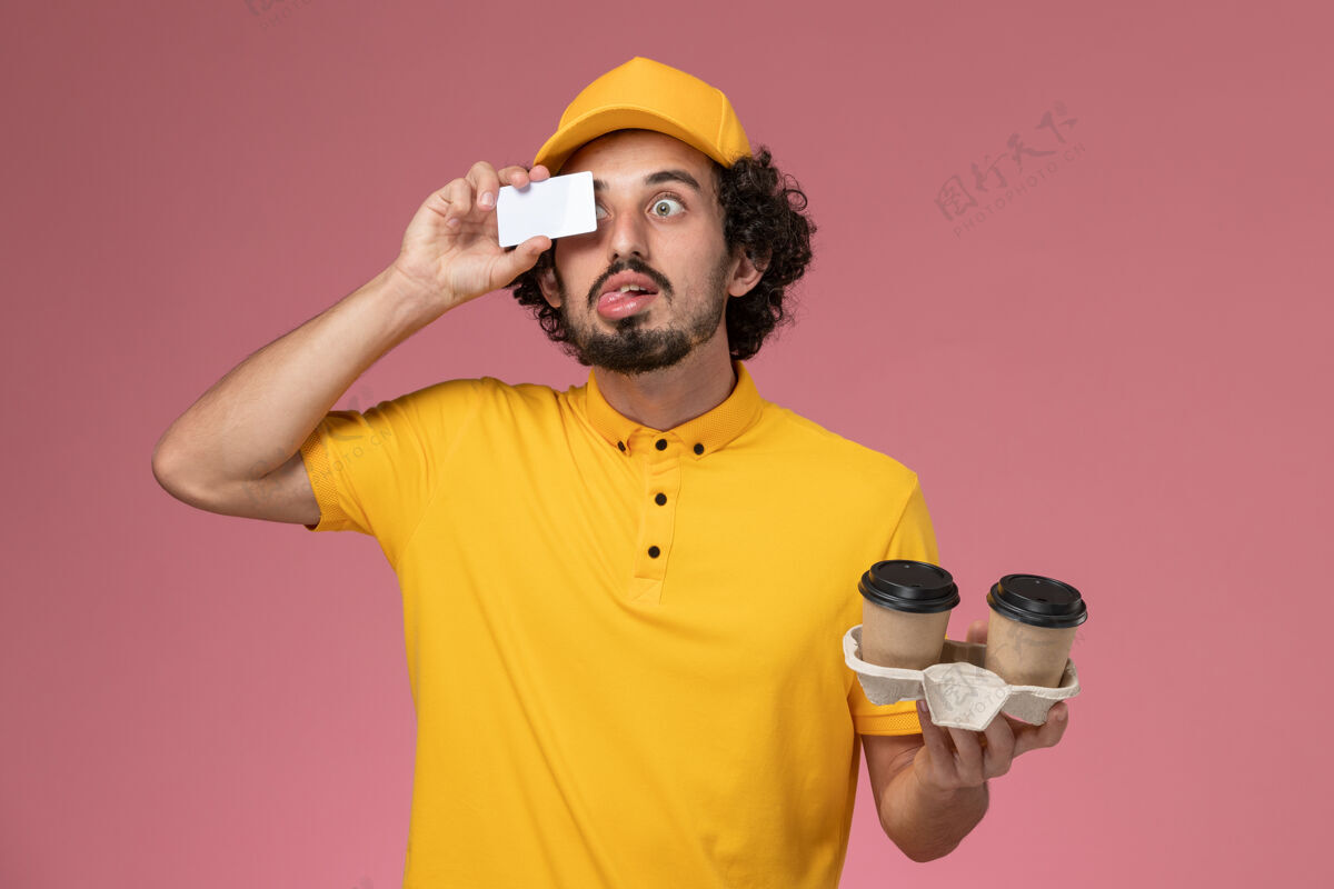 仪器正面图：身穿黄色制服和披风的男性信使手持棕色咖啡杯和粉色墙上的卡片光学模特服务
