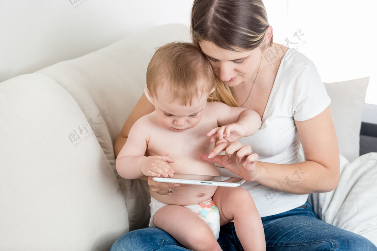 休闲集中的男婴和年轻母亲的肖像触摸屏上的平板电脑女性家庭游戏